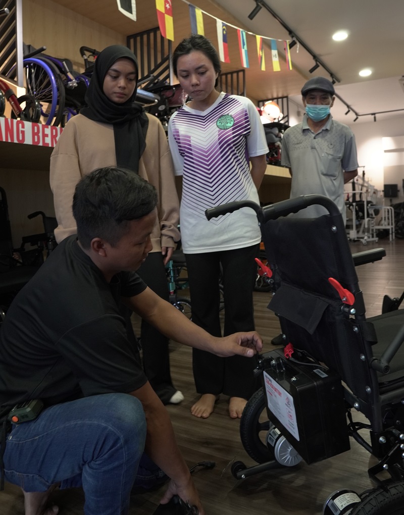 Technician shows electric wheelchair battery to potential buyers in Malaysia. Electric wheelchair test.