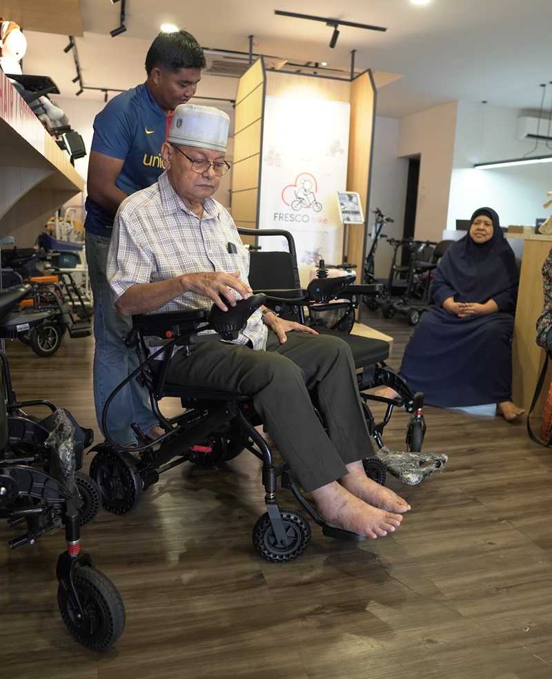 Senior man testing an electric wheelchair in a Malaysian store. Wheelchair test drive.