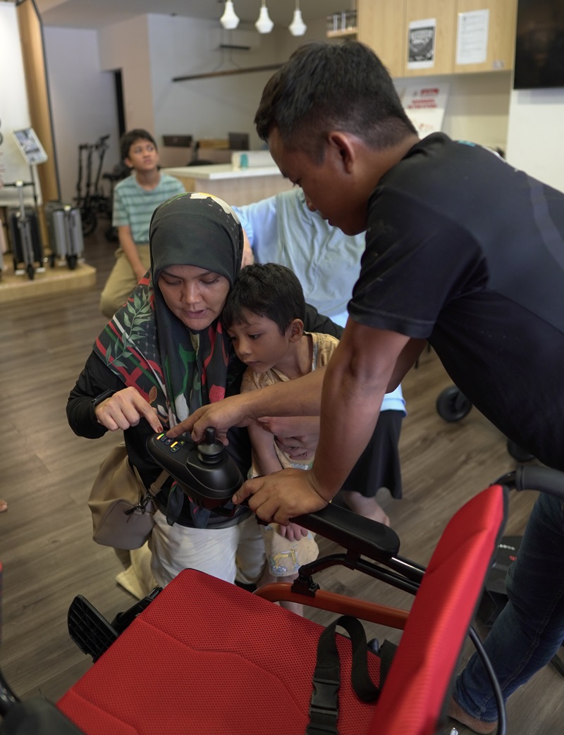 Family testing electric wheelchair controls with salesperson in Malaysia.