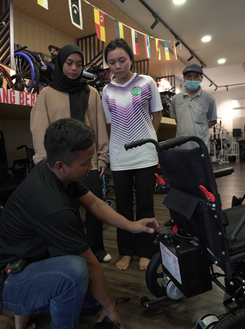 Technician shows customers how to test an electric wheelchair battery before buying in Malaysia.