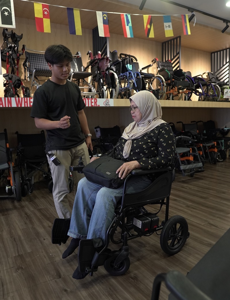 Salesperson assisting customer test drive an electric wheelchair in a Malaysian store. Electric wheelchair test.