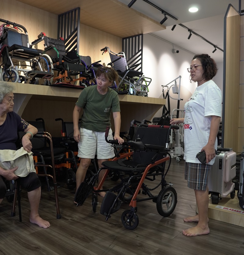 Senior woman & caregivers testing electric wheelchairs in a Malaysia store. Electric wheelchair test drive.