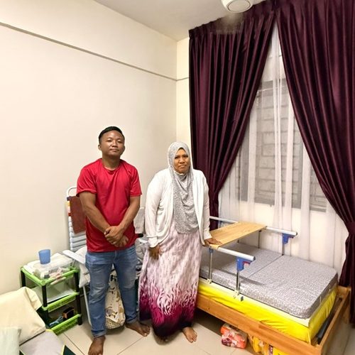Man and woman stand beside a hospital bed with side rails in a bedroom.