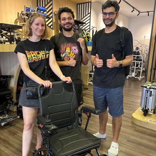Three people in a mobility scooter store, one woman standing beside a new electric wheelchair.