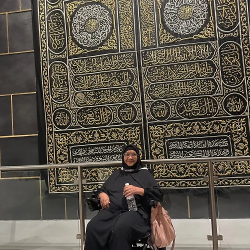 Woman in wheelchair admiring replica Kiswah, Kaaba's embroidered cloth. Islamic pilgrimage.